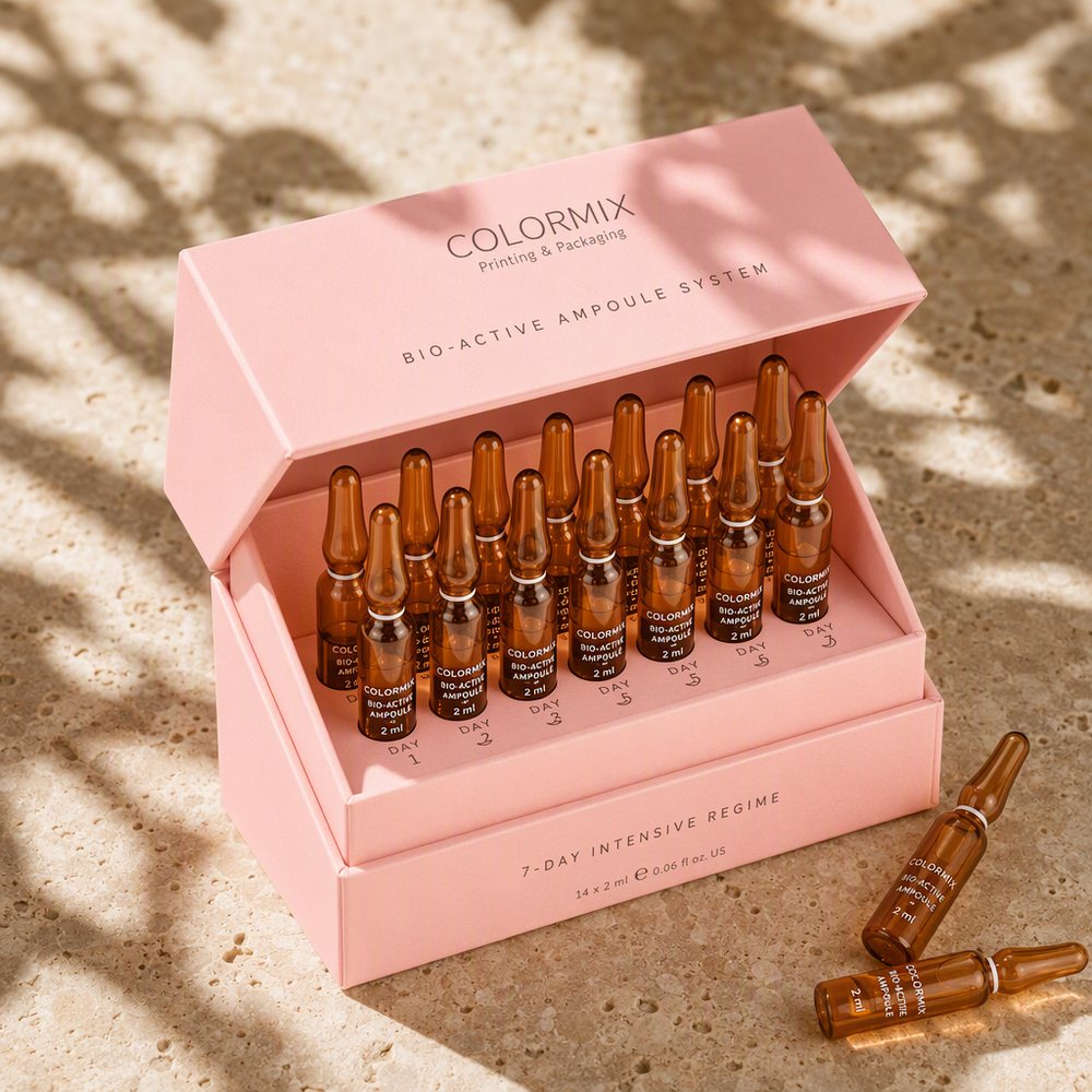 Pink rigid ampoule box open to show fourteen glass serum ampoules held in a printed cradle, branded Colormix