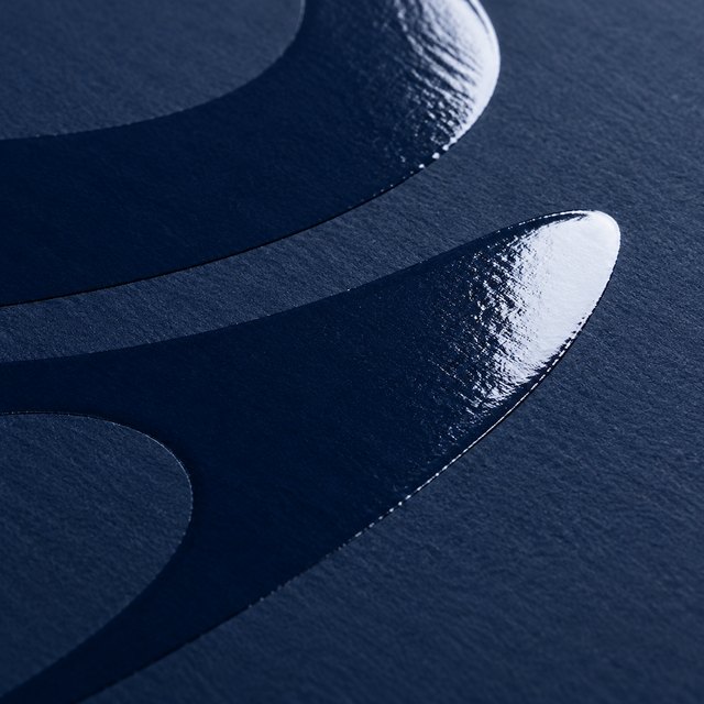 Raised gloss varnish shapes catching light on a matte navy surface