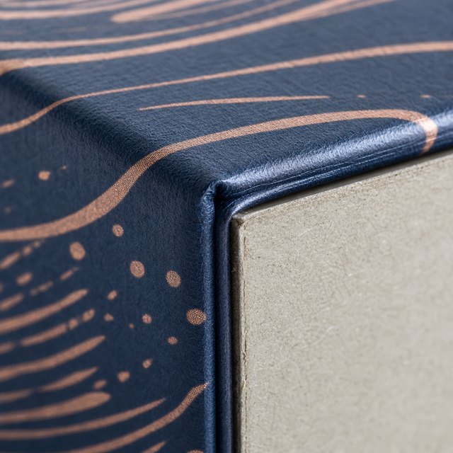 Printed paper wrapped around the corner of a rigid box, board core visible in the fold